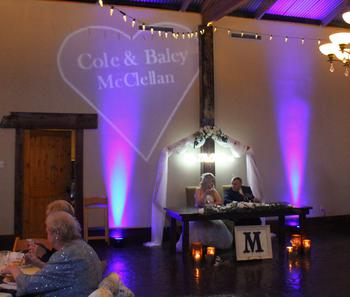 Beautiful blue uplights and name in lights displayed behind the newlyweds: Cole and Baley MCclellan at their wedding reception hosted by DJSean and held at the Barn at the springs in Cave Springs Arkansas.