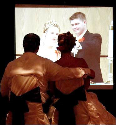 Newlyweds sit, holding hands as they and their guests watch pictures from their childhood and courtship on a 15 foot video screen provided by Sean Hearn with Music In Motion.