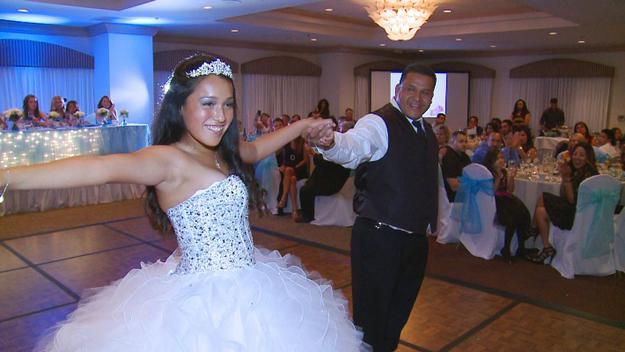A proud father dances with his little princess dressed in a stunning white sequin gown and diamond tiara at at her Quinceanera.