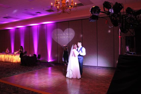 Newlyweds Aaron and Sarah Bushong enjoying first dance at the Inn of the Ozarks with their Name in Lights and beautiful purple uplights in the background.